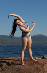 The girl in a bathing suit doing gymnastics on the rock