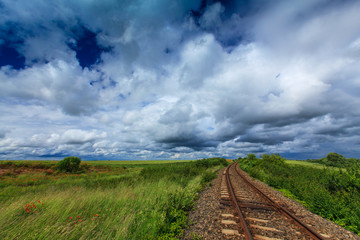 Scenic railroad in rural area in summer with storm clouds