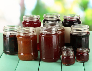 Tasty jam in banks on table on bright background