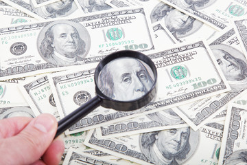 Hand with magnifying glass on a background of dollar bills.