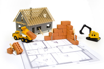 Miniziegelsteine auf Bauplan mit Baufahrzeugen und Haus