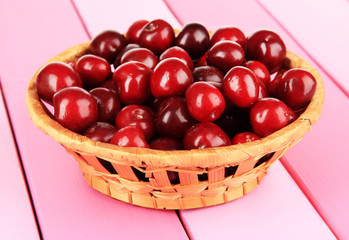 Cherry berries in wicker basket on wooden table close-up