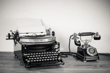 Vintage telephone, old typewriter on table desaturated photo