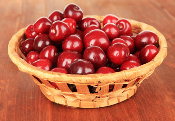 Cherry berries in wicker basket on wooden table close-up