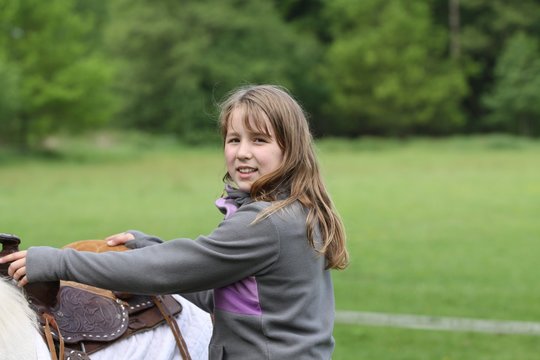 Mädchen steigt auf gesatteltes Pferd