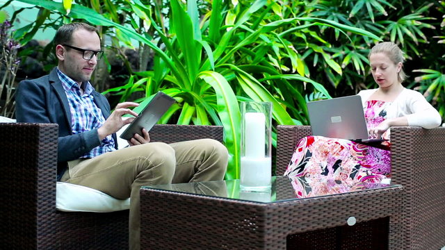 Happy young couple in exotic garden working with tablet and lapt