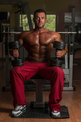 Fototapeta na wymiar shirtless body builder posing with dumbbell at the bench