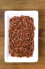 red rice in white bowl on wooden background
