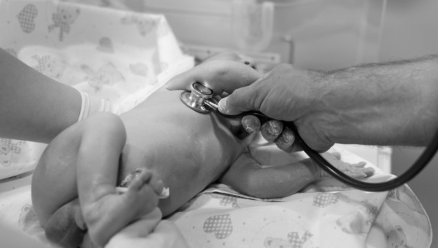 Doctor using a stethoscope to listen to a newborn baby's heart. 