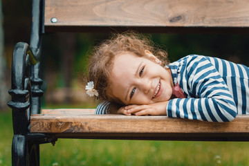 Portrait of little girl lying on bench in a park