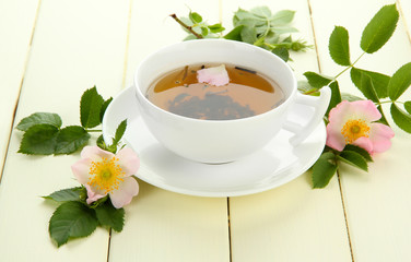 Cup of herbal tea with hip rose flowers on white wooden table