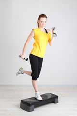 Beautiful young woman exercises with dumbbell on stepper