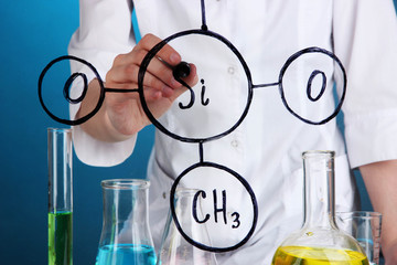 Fototapeta premium Chemist woman writing formulas on glass on blue background