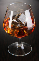 Brandy glass with ice on wooden background