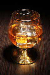 Brandy glass with ice on wooden background