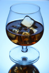 Brandy glass with ice on blue background