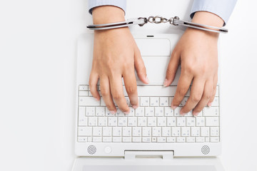 Female hands in handcuffs, with laptop - obrazy, fototapety, plakaty