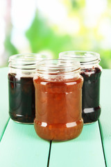 Tasty jam in banks on table on bright background