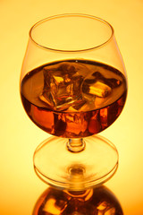 Brandy glass with ice on yellow background