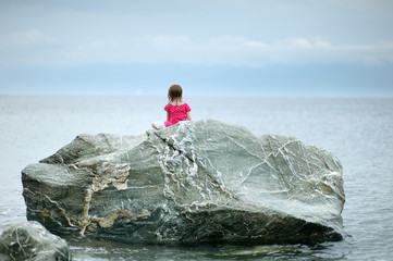 Adorable little girl sitting on a rock