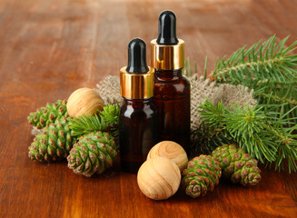 Bottles of fir tree oil and green cones on wooden background