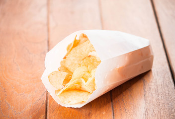 Potato chips in paper pack on wood table