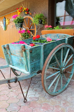 Bemalter Holzkarren mit Blumenschmuck vor einem Haus