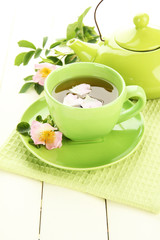 Cup and teapot of herbal tea with hip rose flowers
