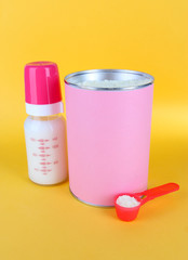 Powdered milk with baby bottle of milk on yellow background