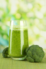 Glass of broccoli juice, on bamboo mat, on green background