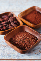 cocoa beans, powder and grated chocolate in wooden bowls, white