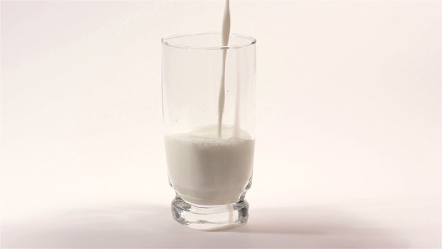 Milk flowing in  transparent cup on  white background