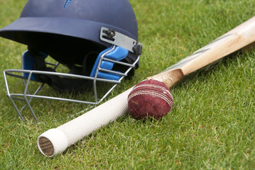 Cricket ball, bat and helmet on green grass of cricket pitch