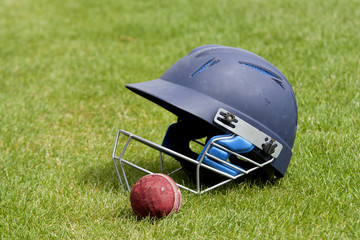 Cricket ball, bat and helmet on green grass of cricket pitch