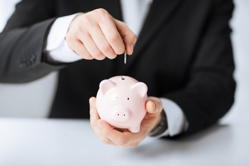 man putting coin into small piggy bank