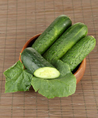 Tasty green cucumbers in wooden bowl, on bamboo mat background