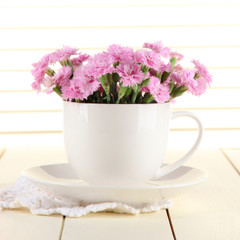 Many small pink cloves in cup on wooden background