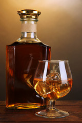 Brandy with ice on wooden table on brown background