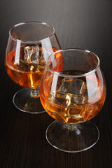 Brandy glasses with ice on wooden background