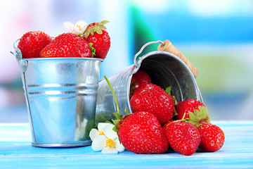 Ripe sweet strawberries in metal pails on blue wooden table