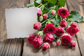 Pink roses and white card with a place for a text on a wooden ta