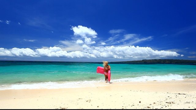 Woman with pink swimming mattress on caribbean beach