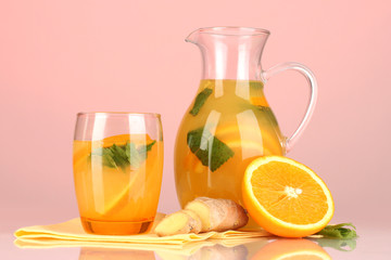 Orange lemonade in pitcher and glass on pink background