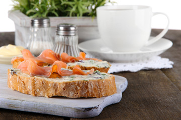 Fish sandwiches and cup of tea on cutting board on wooden table