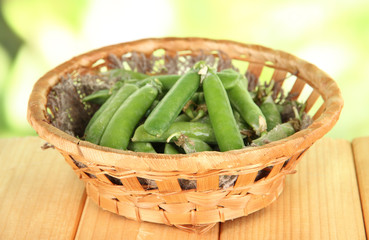 Green peas in basket on wooden table on nature background