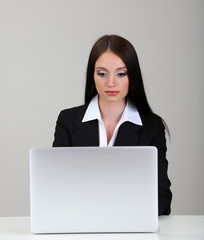 Young business woman working with computer, on gray background