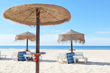 Sunny beach in Portugal with wooden umbrellas near the sea. Summ