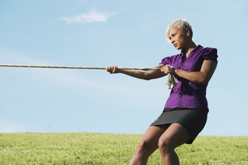 competitive businesswoman playing tug of war with rope