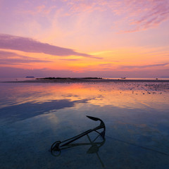 Sunset seascape, old anchor in water during ebb