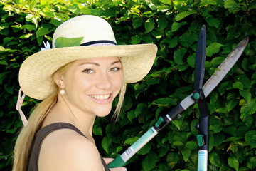 Junge Frau im Garten schneidet Hecke mit Heckenschere